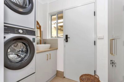 Port Noarlunga South laundry renovation Renovated laundry with white cabinetry, brass handles and a stacked washer and dryer